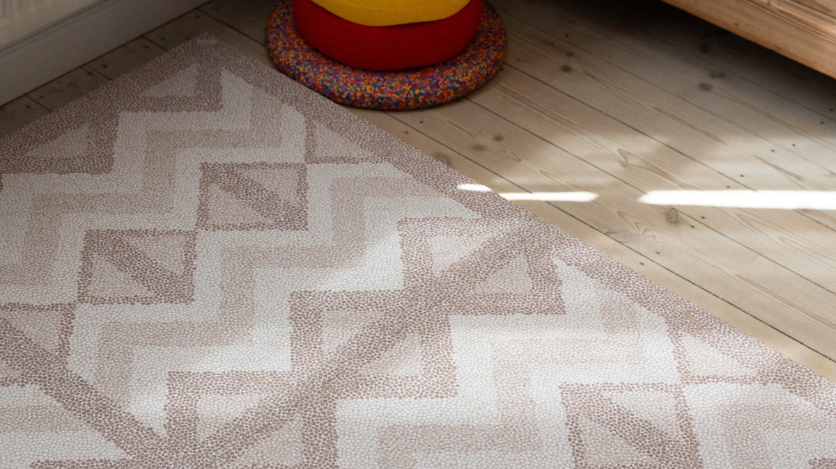 Foam play mat with a muted geometric pattern laid in the corner of a room with wood flooring