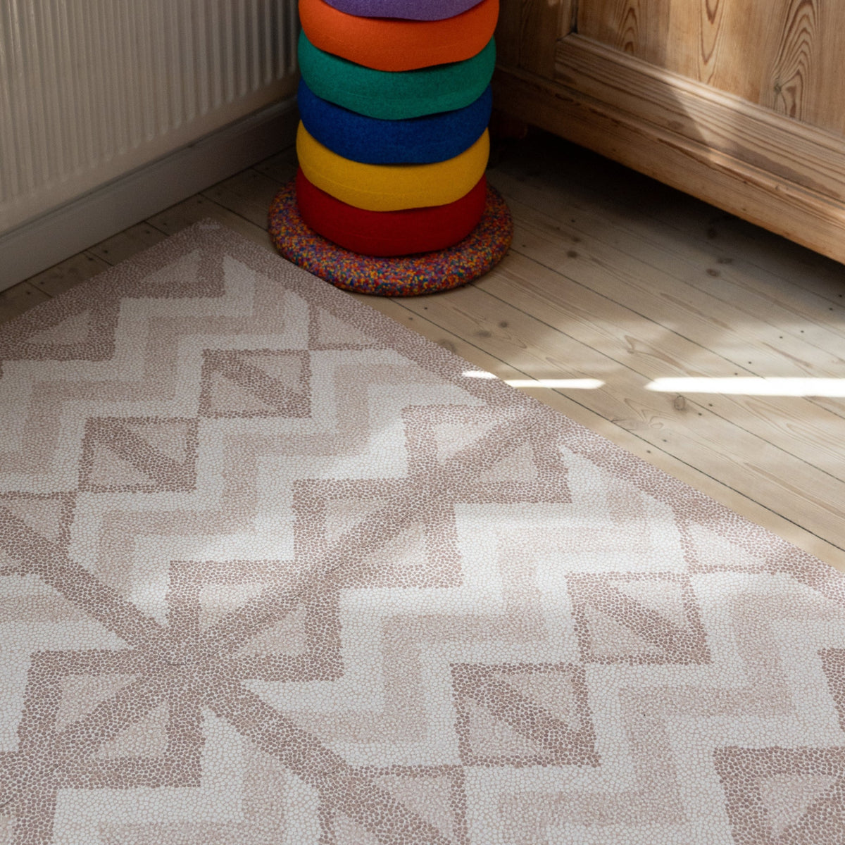 Foam play mat with a muted geometric pattern laid in the corner of a room with wood flooring