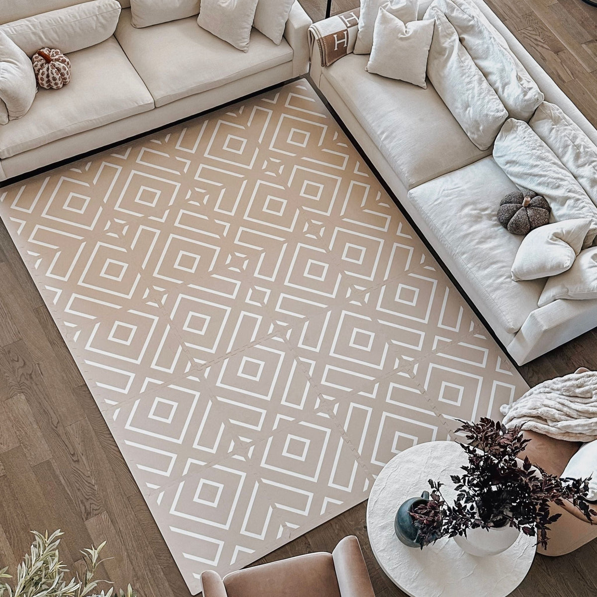 Foam play mat with a pale geometric pattern covering most of a living room floor, seen from above