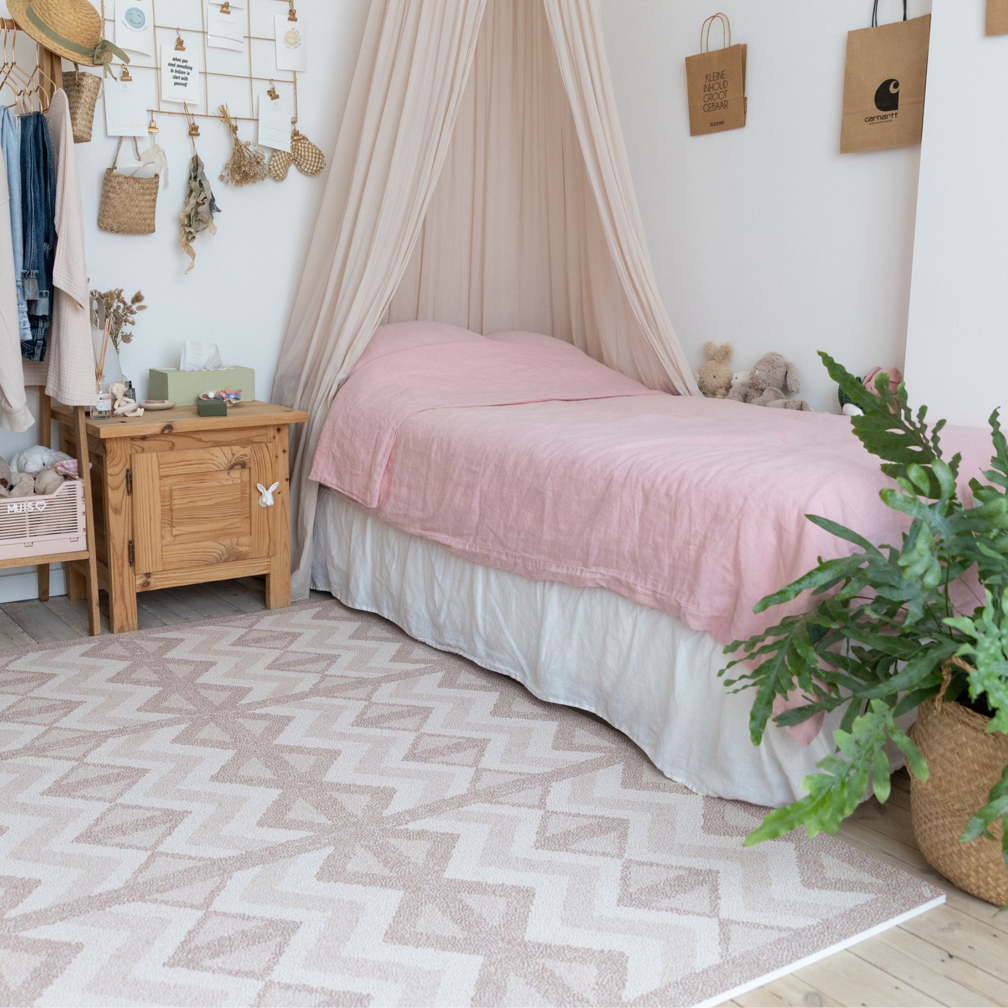 Bedroom with pink bedspread, wooden nightstand, and patterned rug.